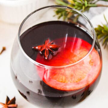 Glass of spiced wine on a white background surrounded by garnishes.