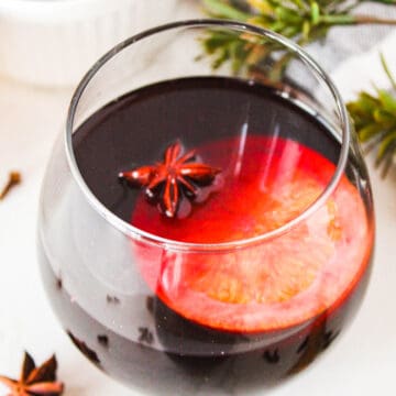 Glass of spiced wine on a white background surrounded by garnishes.