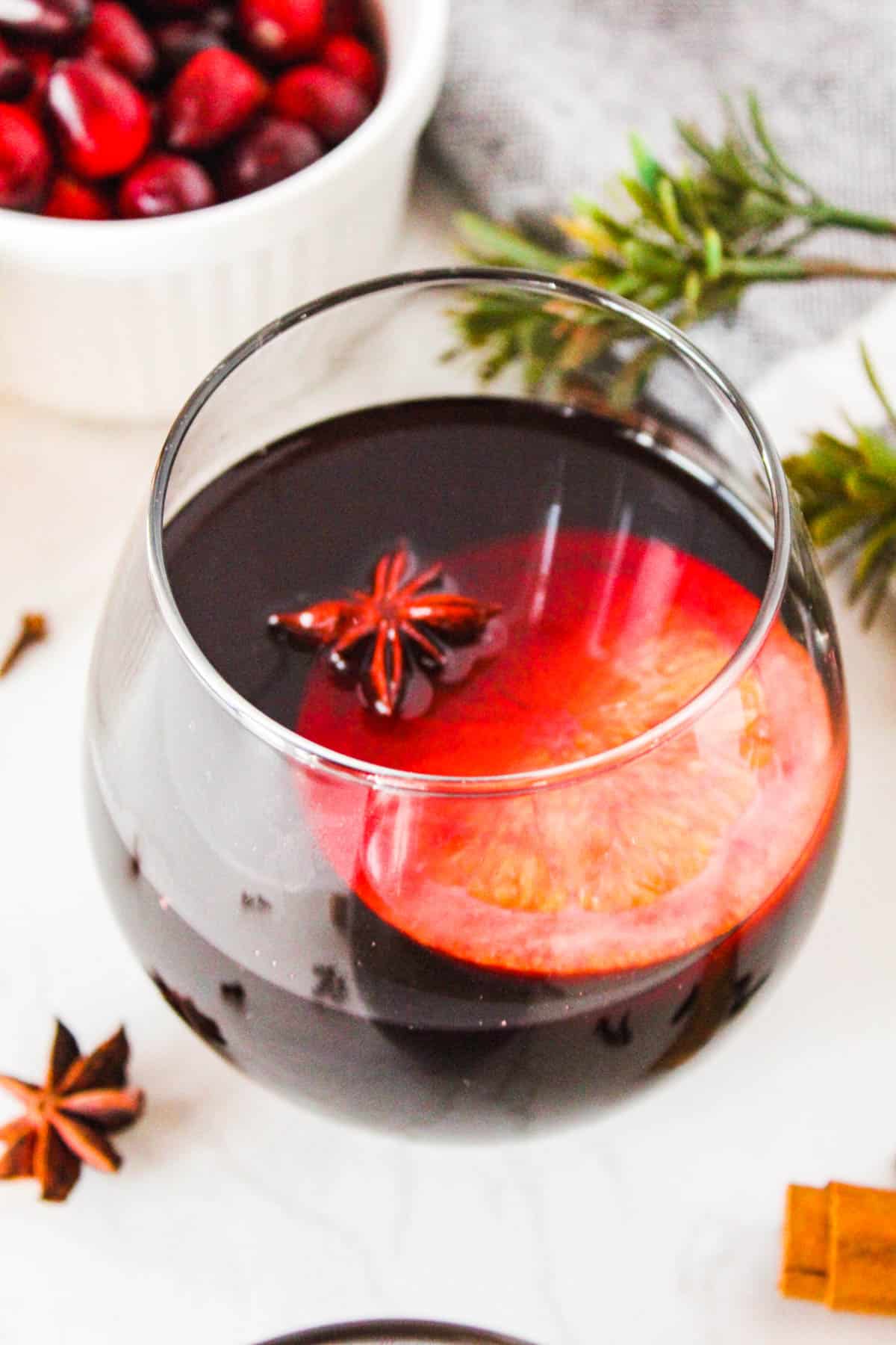 Glass of spiced wine on a white background surrounded by garnishes.