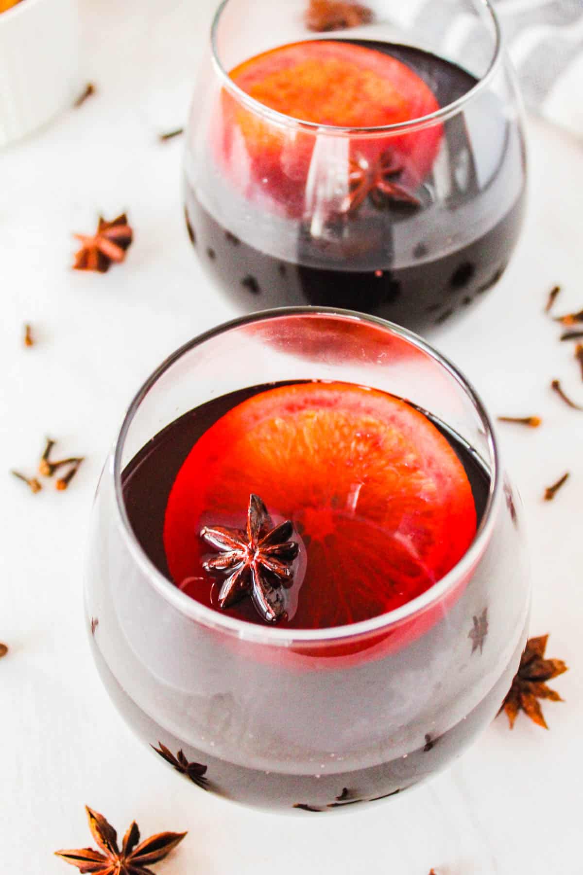 Two glasses of hot spiced wine garnished with orange wheels and star anise.