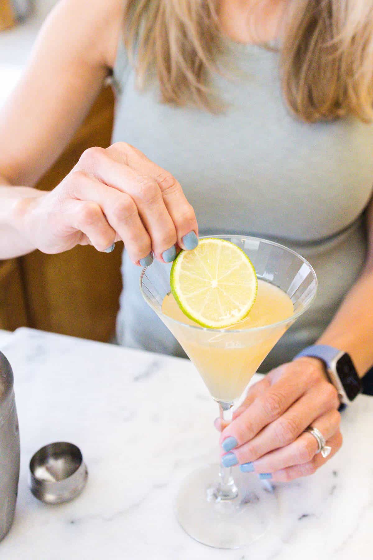 Woman garnishing a martini with a fresh lime wheel.