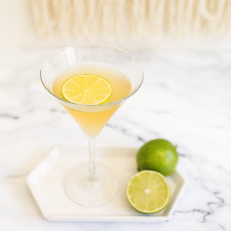 Close up of a tequila martini in a martini glass on a white tray with a cut lime.