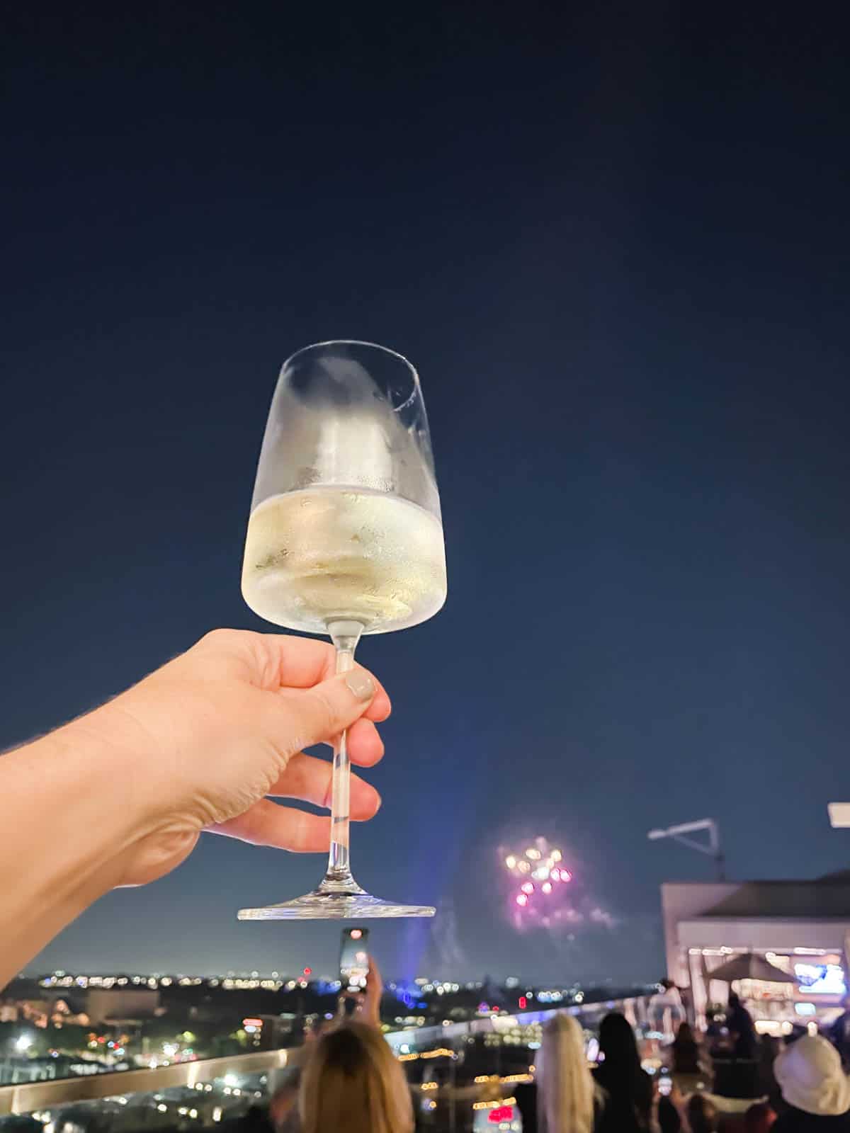 A woman's hand holding white wine on the Parkestry rooftop bar watching Disneyland Fireworks.