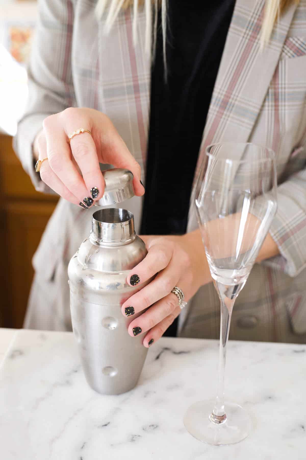 Woman taking the cap off a cocktail shaker next to a champagne flute.