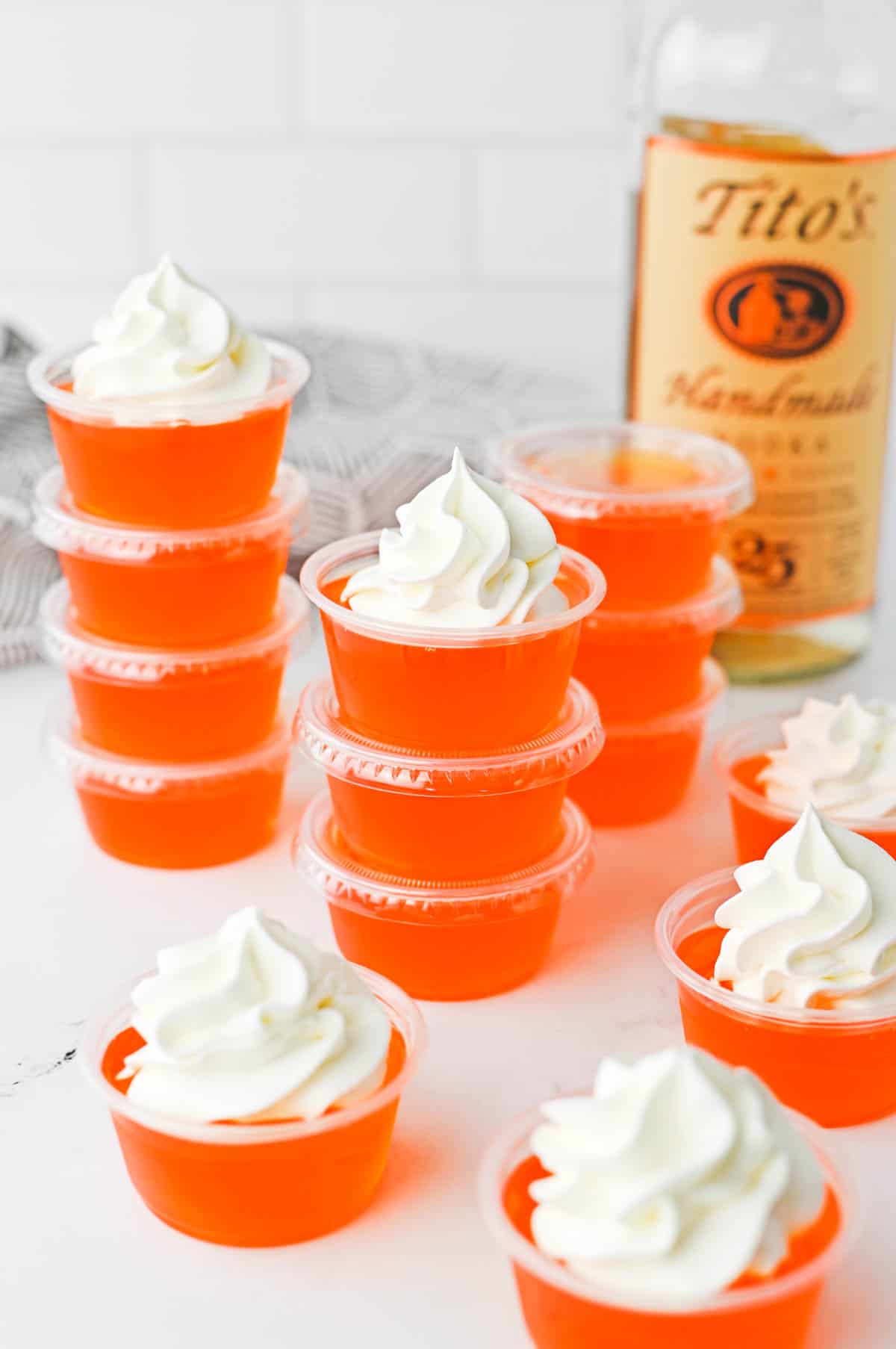 Stacked Jello shots in front of a bottle of vodka topped with whipped cream.