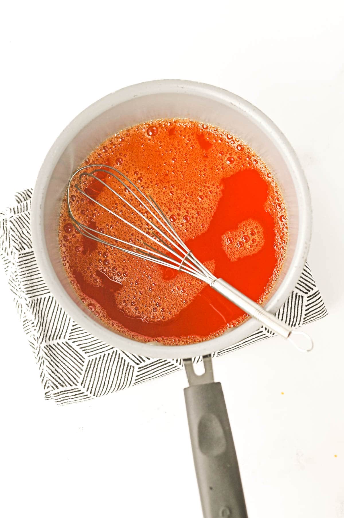 orange jello being whisked in a saucepan