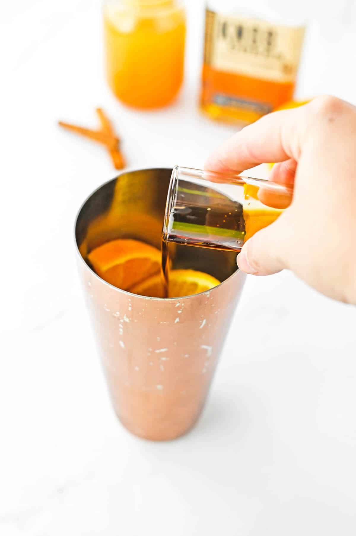 Maple syrup being poured into a copper cocktail shaker.