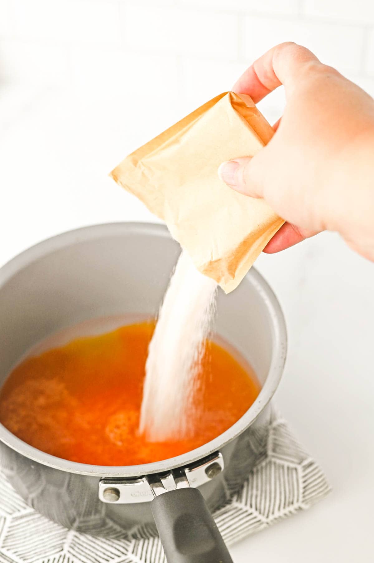 Orange jello being poured into a saucepan.