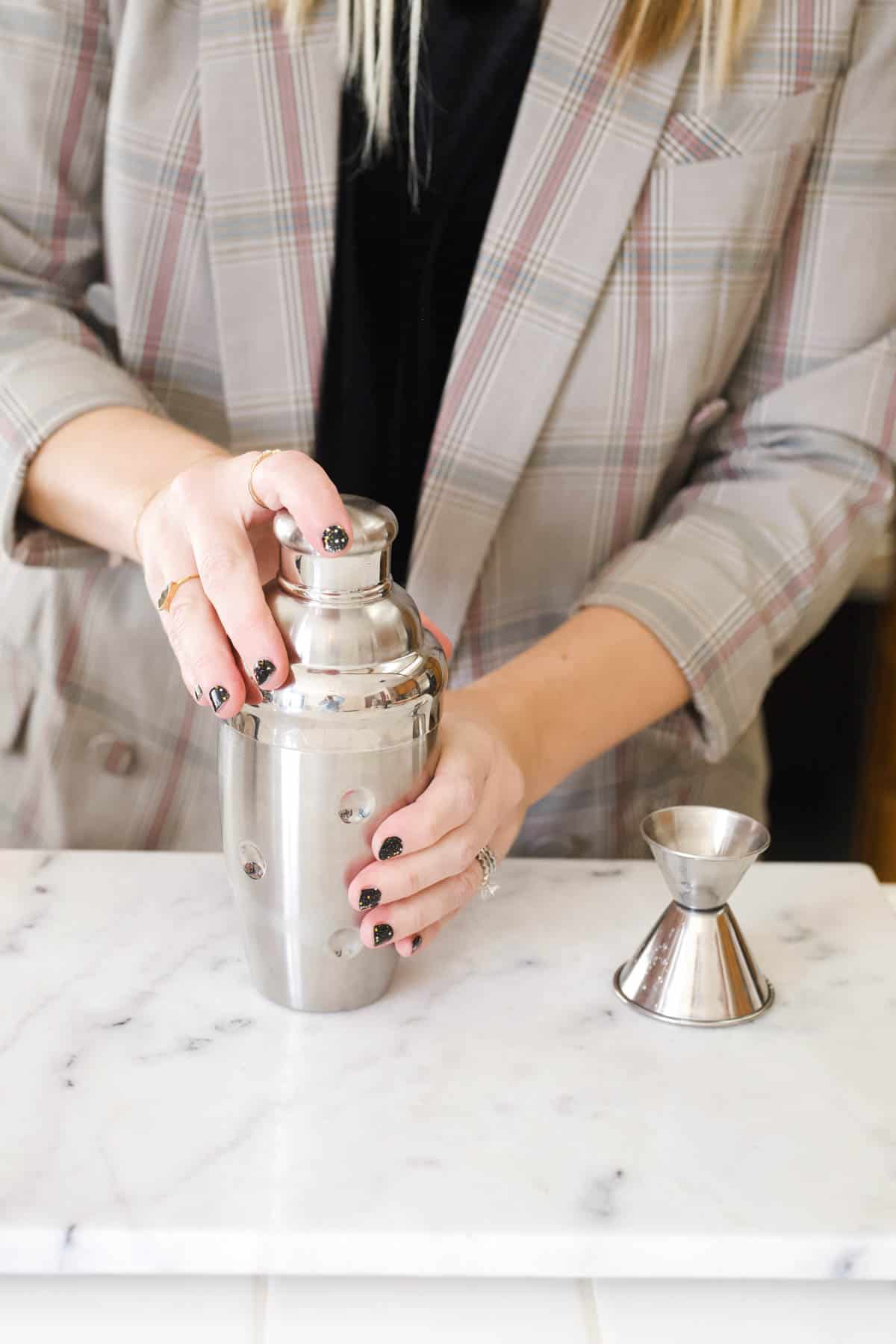 Woman picking up a silver cocktail shaker.