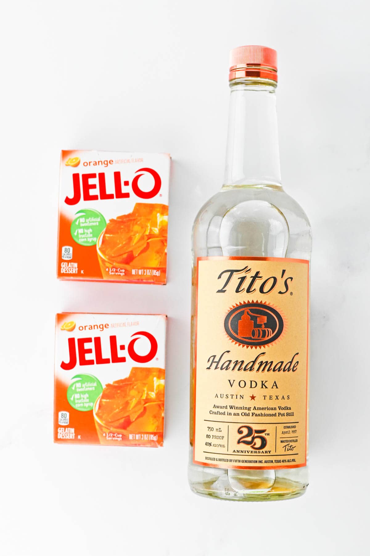 Two packets of orange jello next to a bottle of vodka.