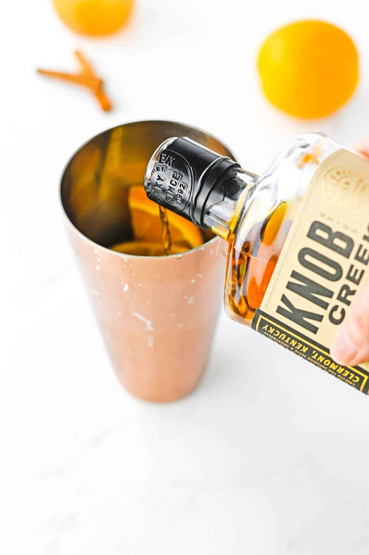 Bourbon being poured into a copper cocktail shaker.