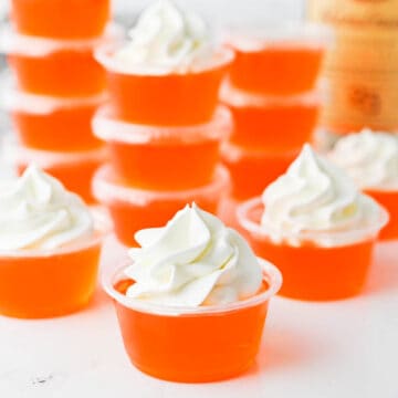 Close up of stacked orange Jello shots topped with whipped cream.