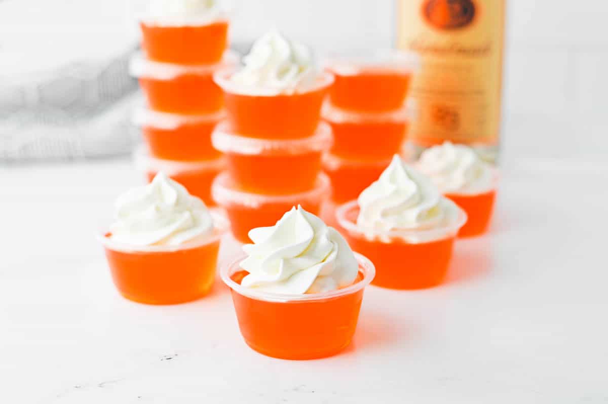 Stacked orange jello shots topped with whipped cream.