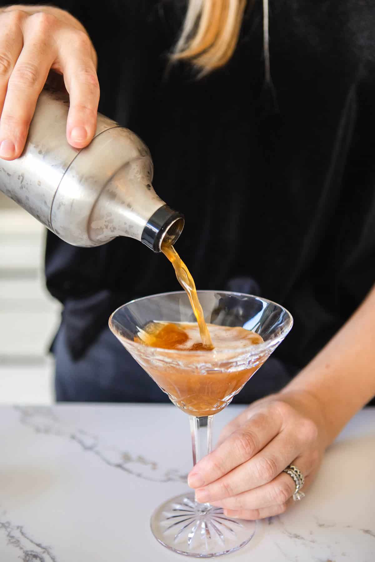 Woman pouring a virgin Espresso Martini into a martini glass from a cocktail shaker.