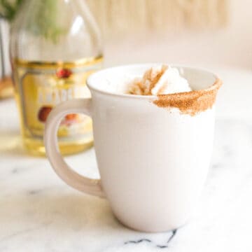 Mug of coffee topped with whipped cream dipped in cinnamon.