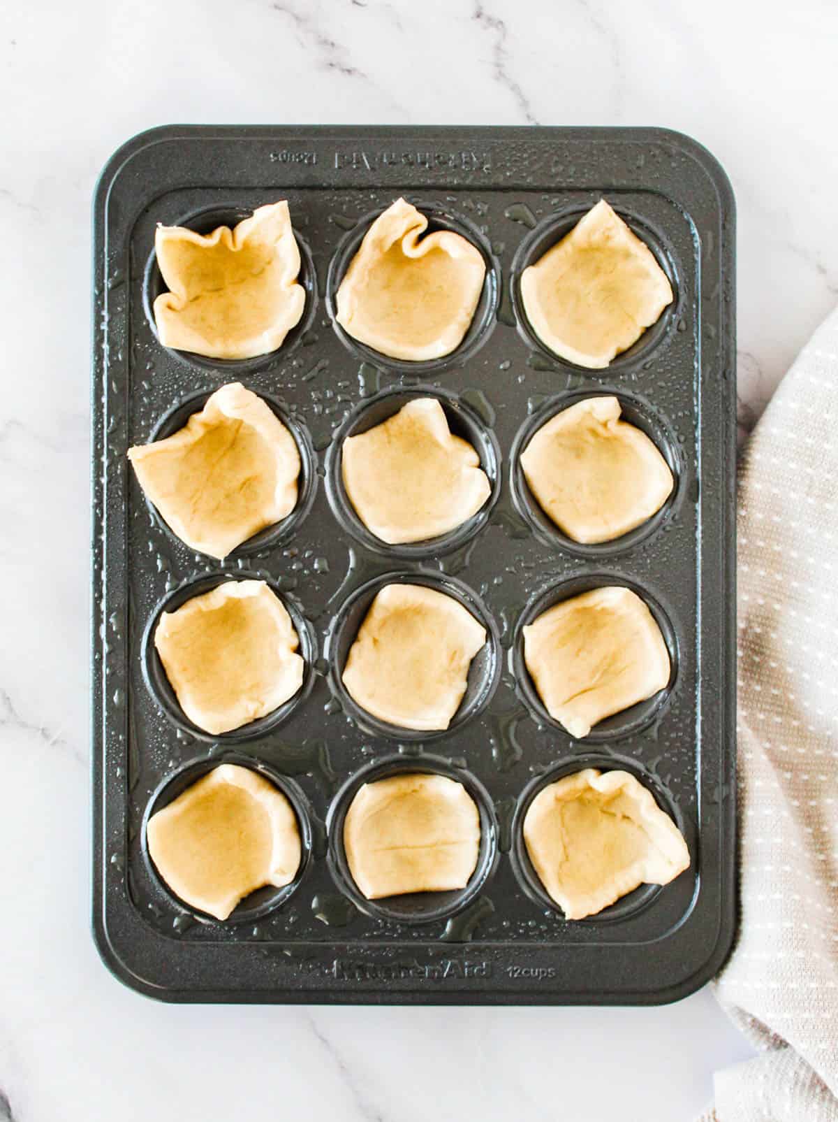 Crescent roll dough pressed on mini muffin tin slots to make brie cranberry bites.