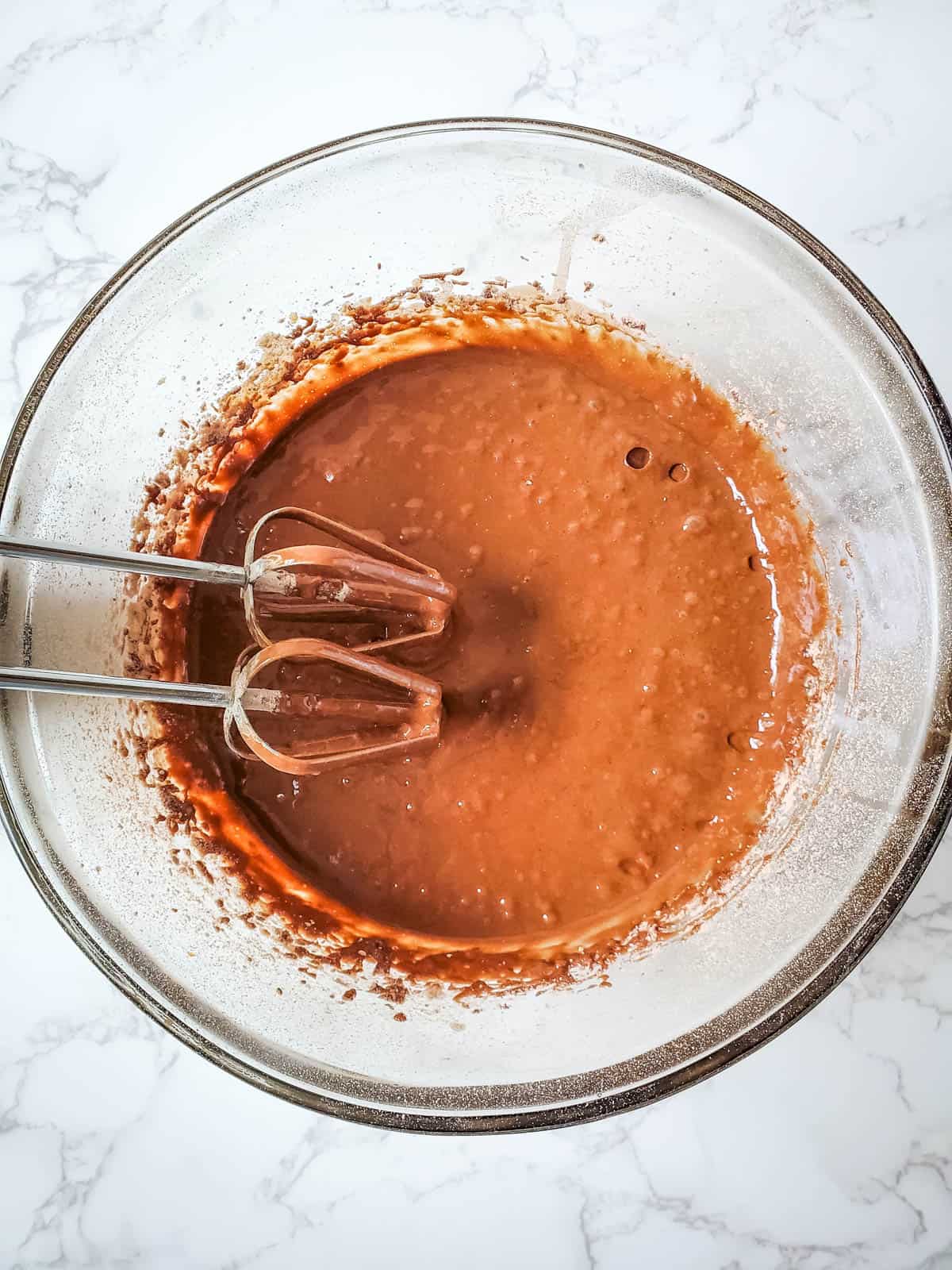 Snickers cupcakes batter on a glass mixing bowl mixed using a hand mixer with whisk attachment.