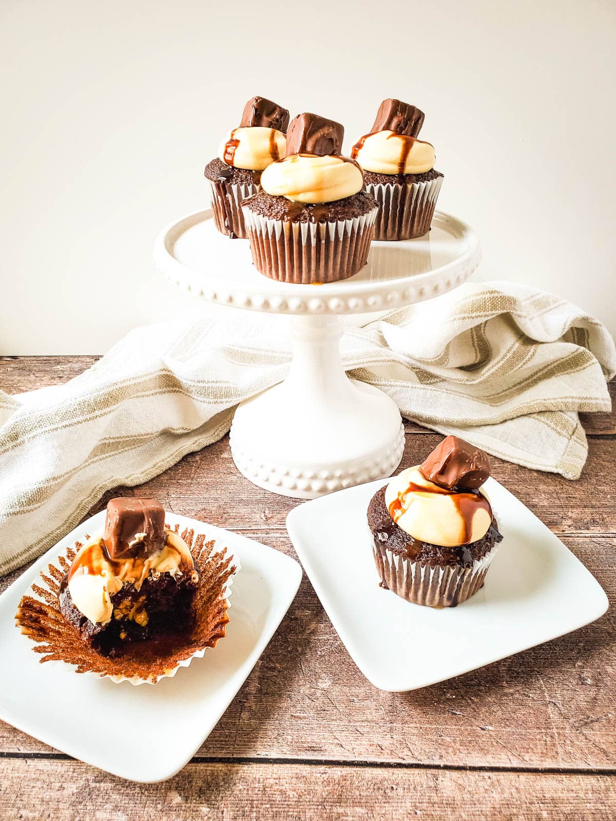 Three chocolate cupcakes stuffed with caramel and peanuts on a cake stand and two on serving plates.
