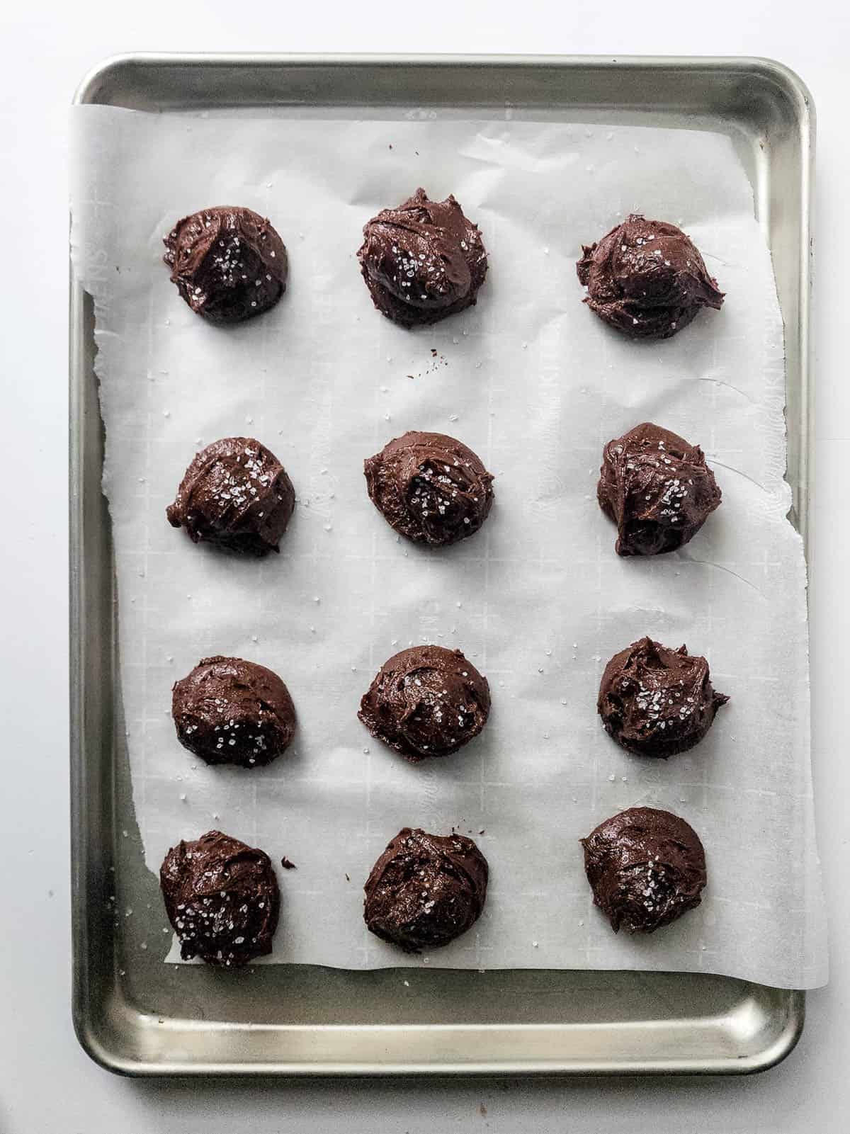 Brownie cookie dough scooped on a parchment paper lined baking sheet.