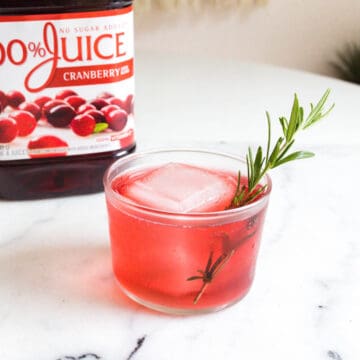 Close up of a cranberry juice drink garnished with a fresh rosemary sprig.