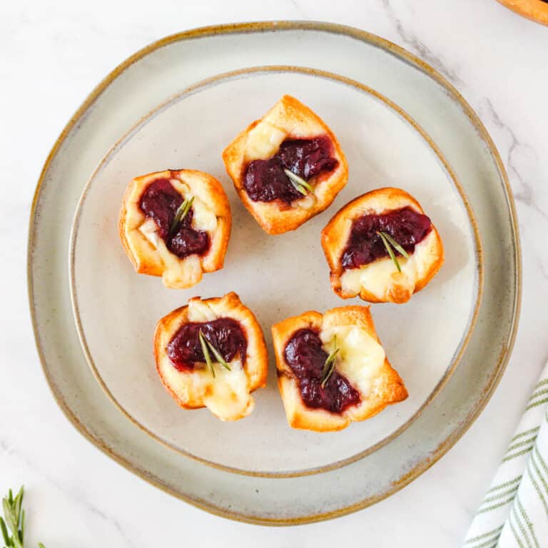 Five baked cranberry brie bites on a presentation plate.