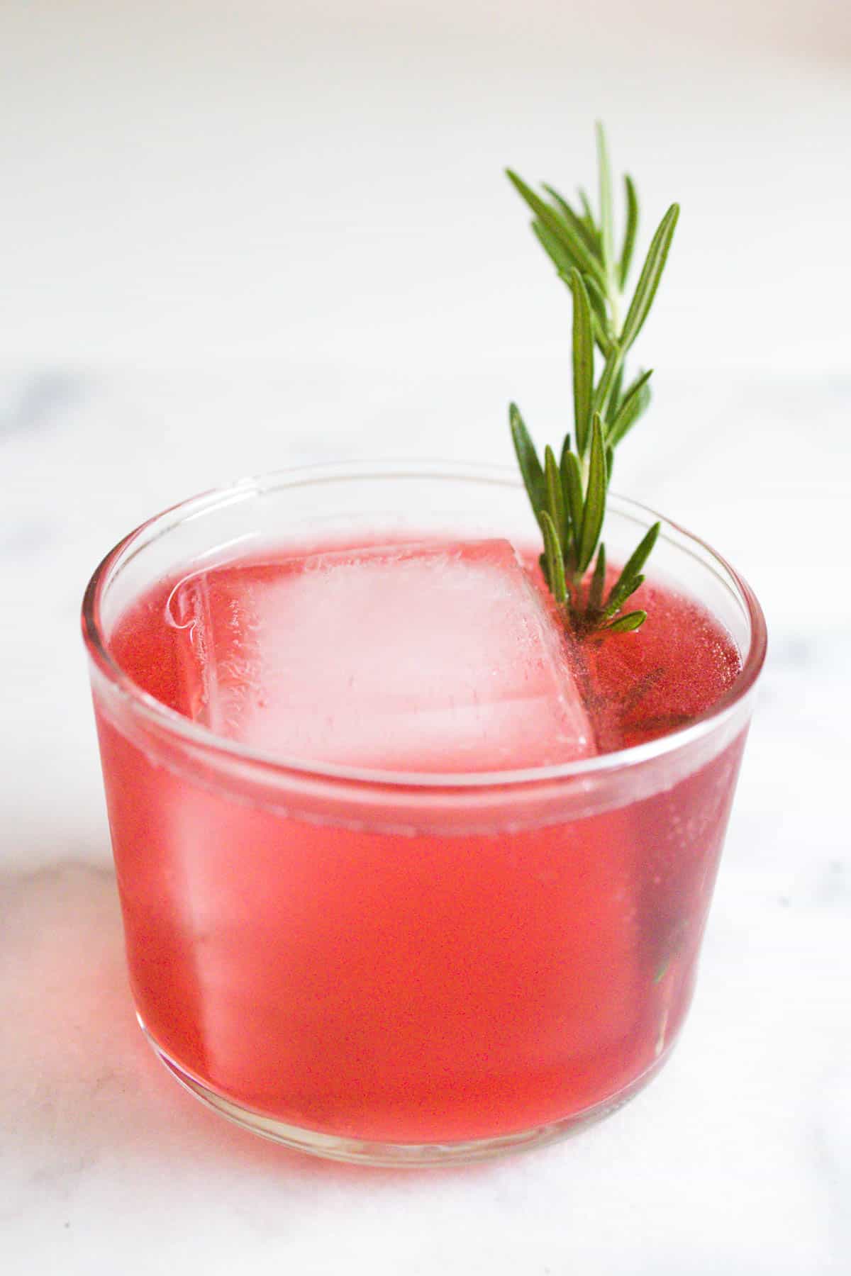 Close up of a cranberry and tequila cocktail on a white marble countertop.
