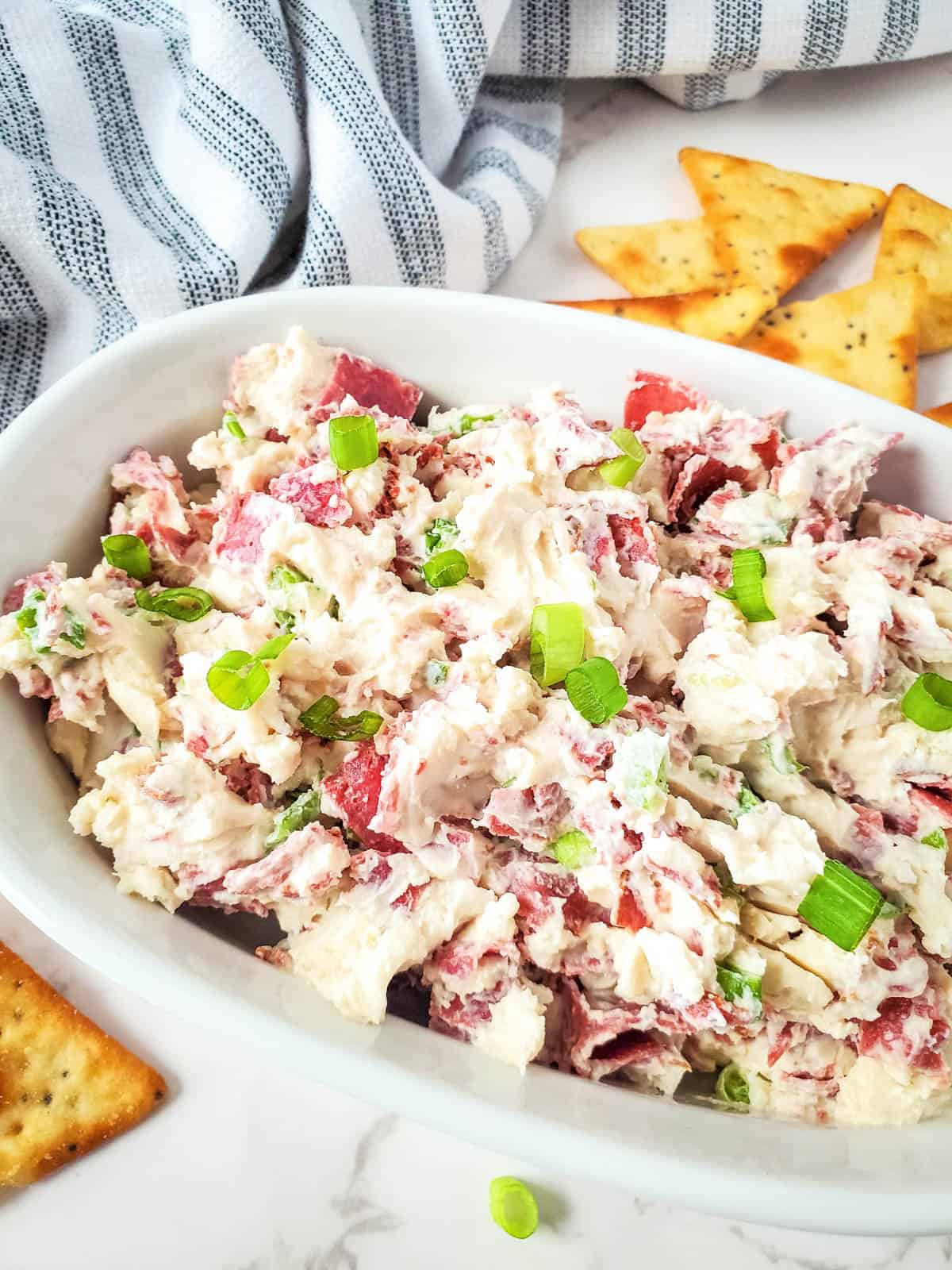 Delicious dried beef cream cheese dip with crackers and a striped towel on the side.