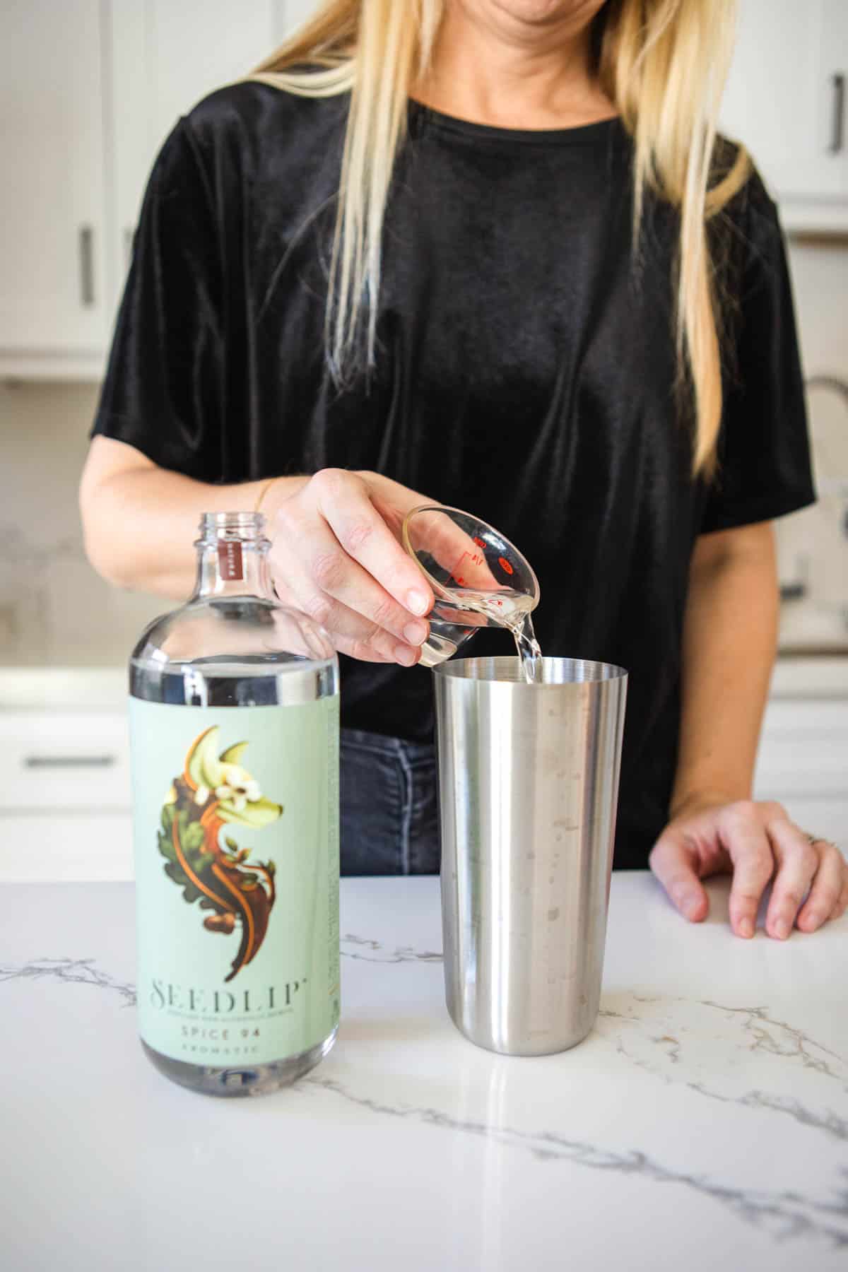 A woman adding Seedlip 94 to a cocktail shaker to make a virgin non alcoholic espresso Martini.