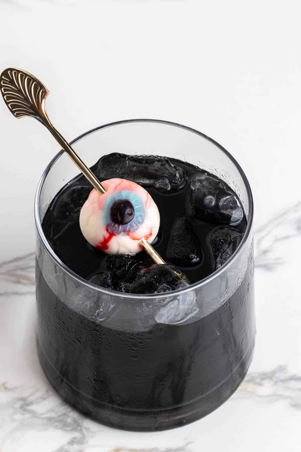 A close up of a black cocktail with a gummy eyeball garnish for Halloween.