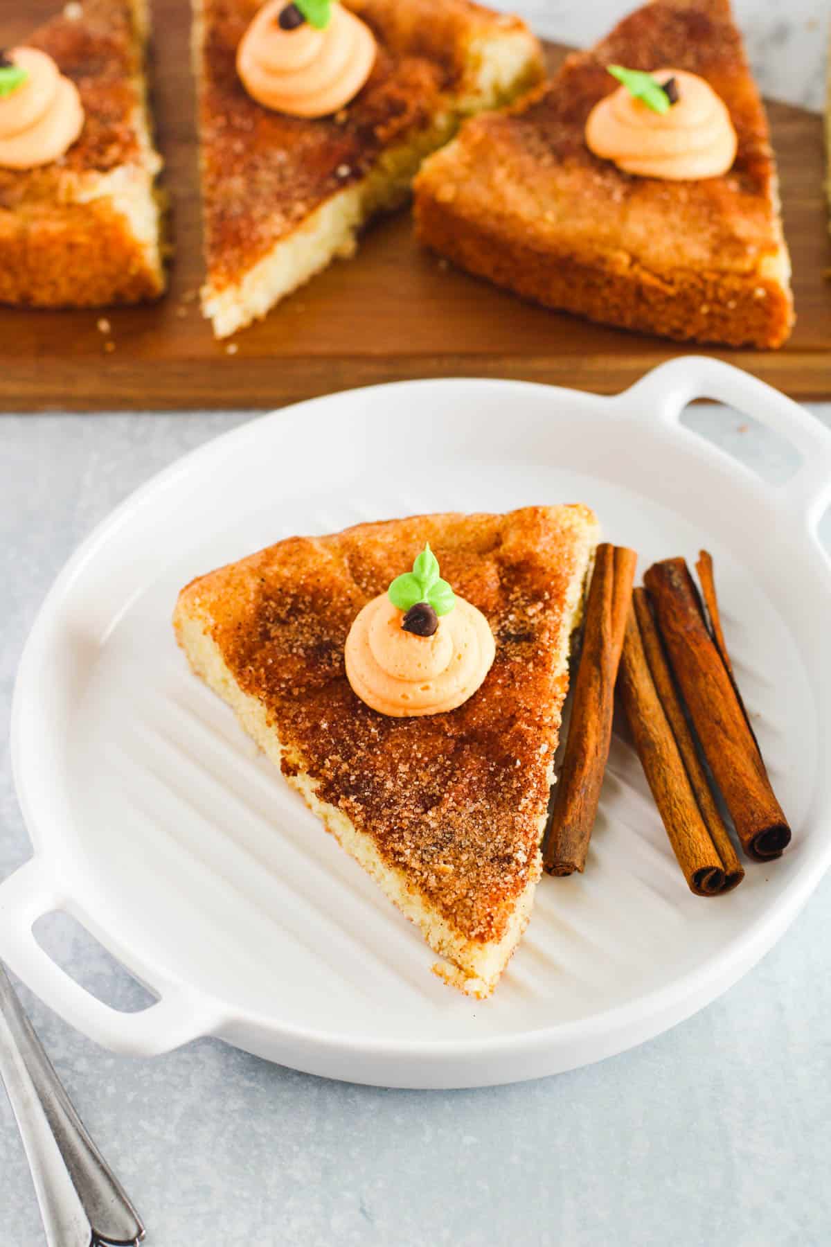 A slice of Snickerdoodle cookie cake on a plate decorated with a frosting pumpkin on top. 