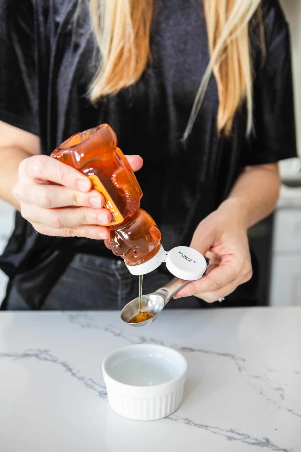 Woman squeezing honey into a small glass dish.