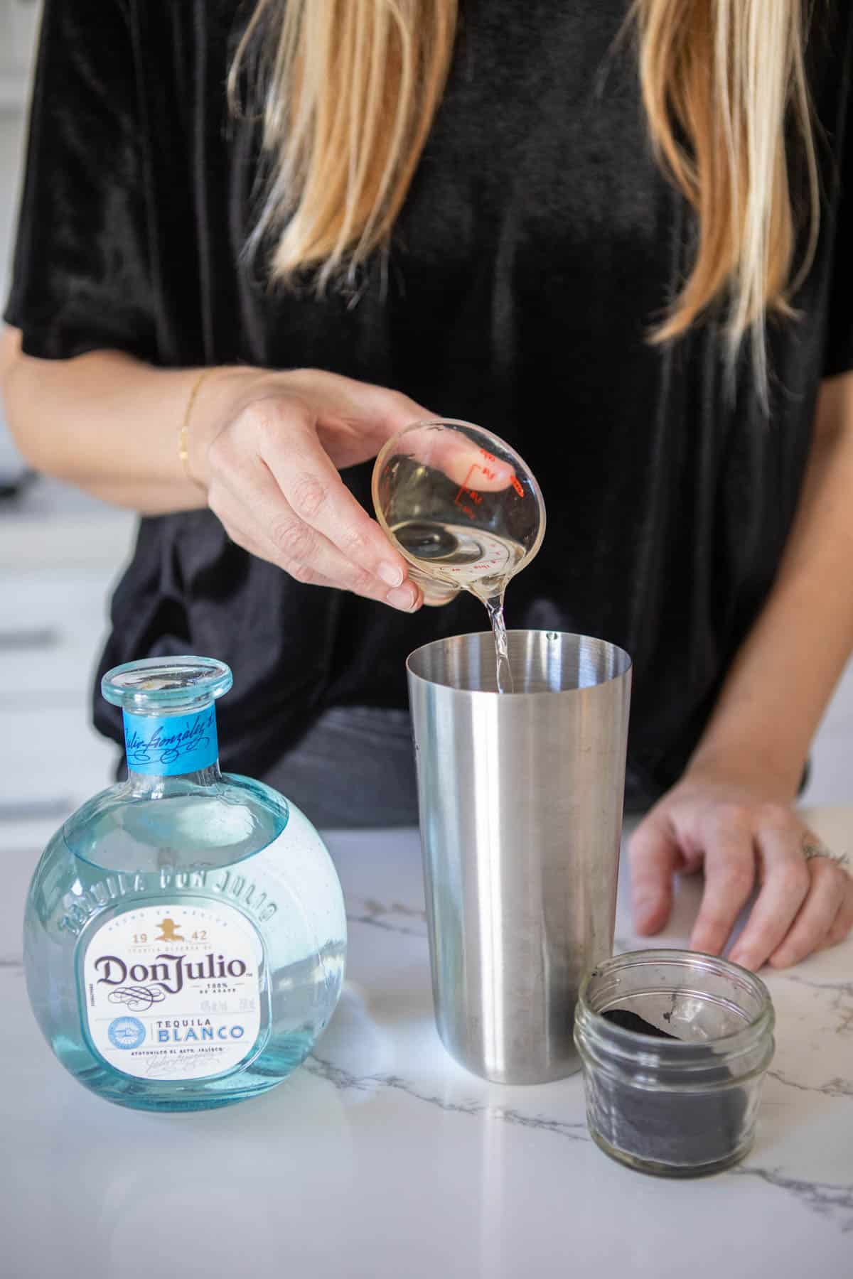 Woman adding tequila to a cocktail shaker.
