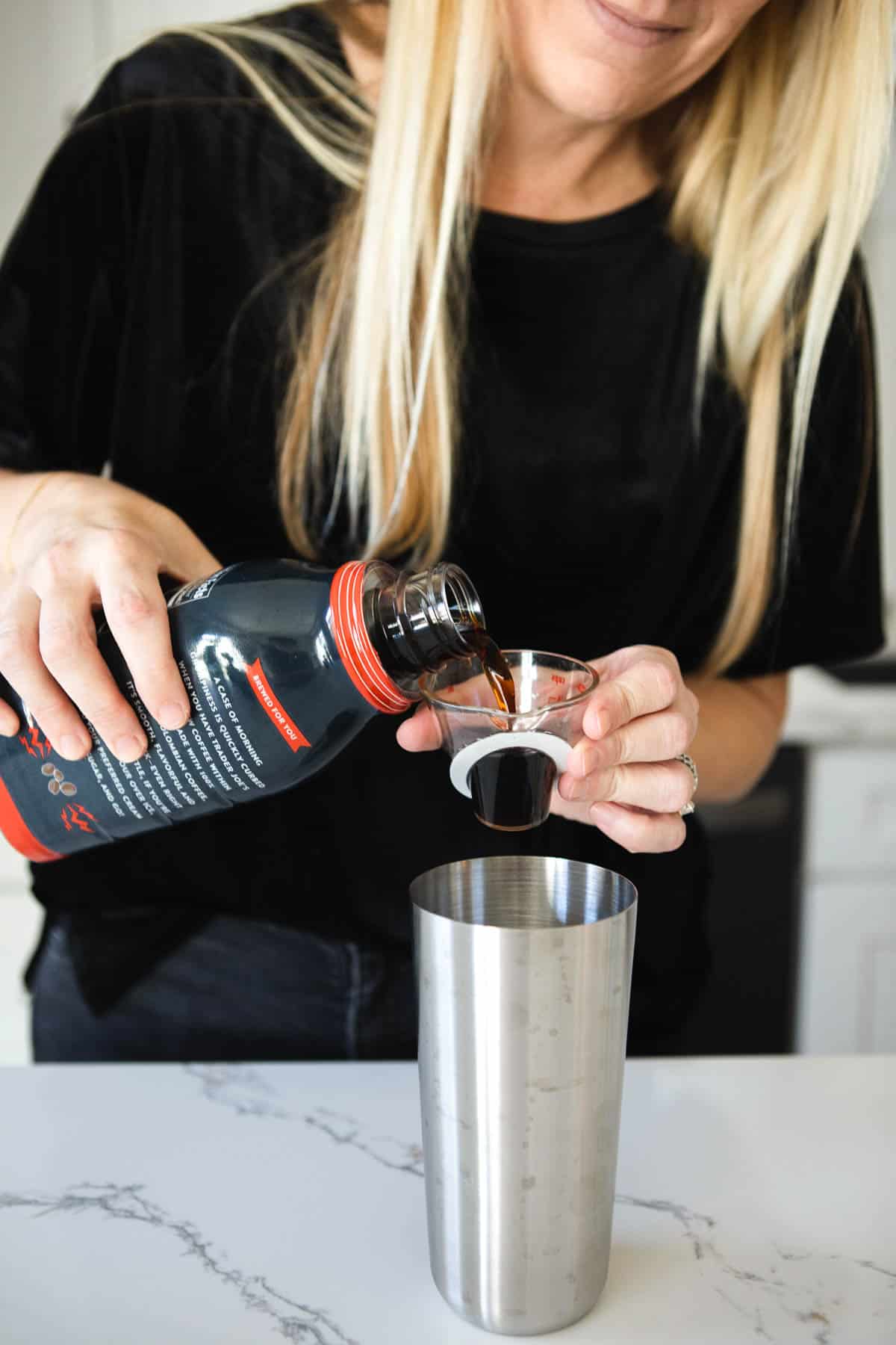 Woman measuring cold brew espresso into a cocktail shaker.