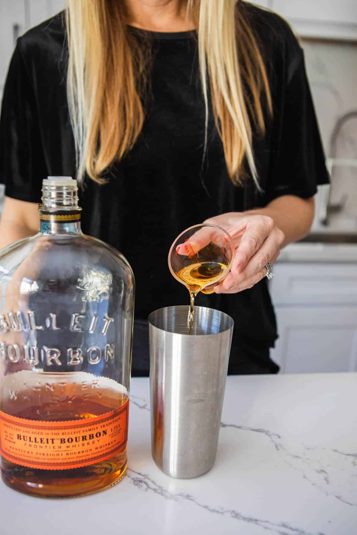 Woman measuring bourbon into a cocktail shaker.