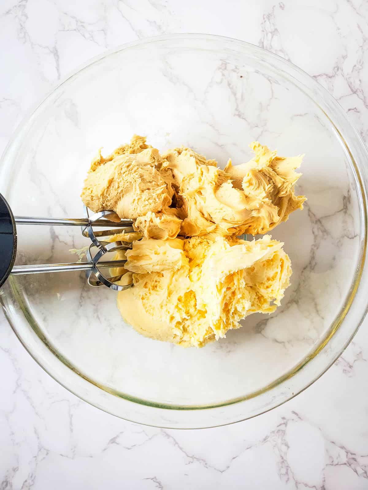 Whipping up salted caramel and vanilla buttercream frosting in a glass bowl.