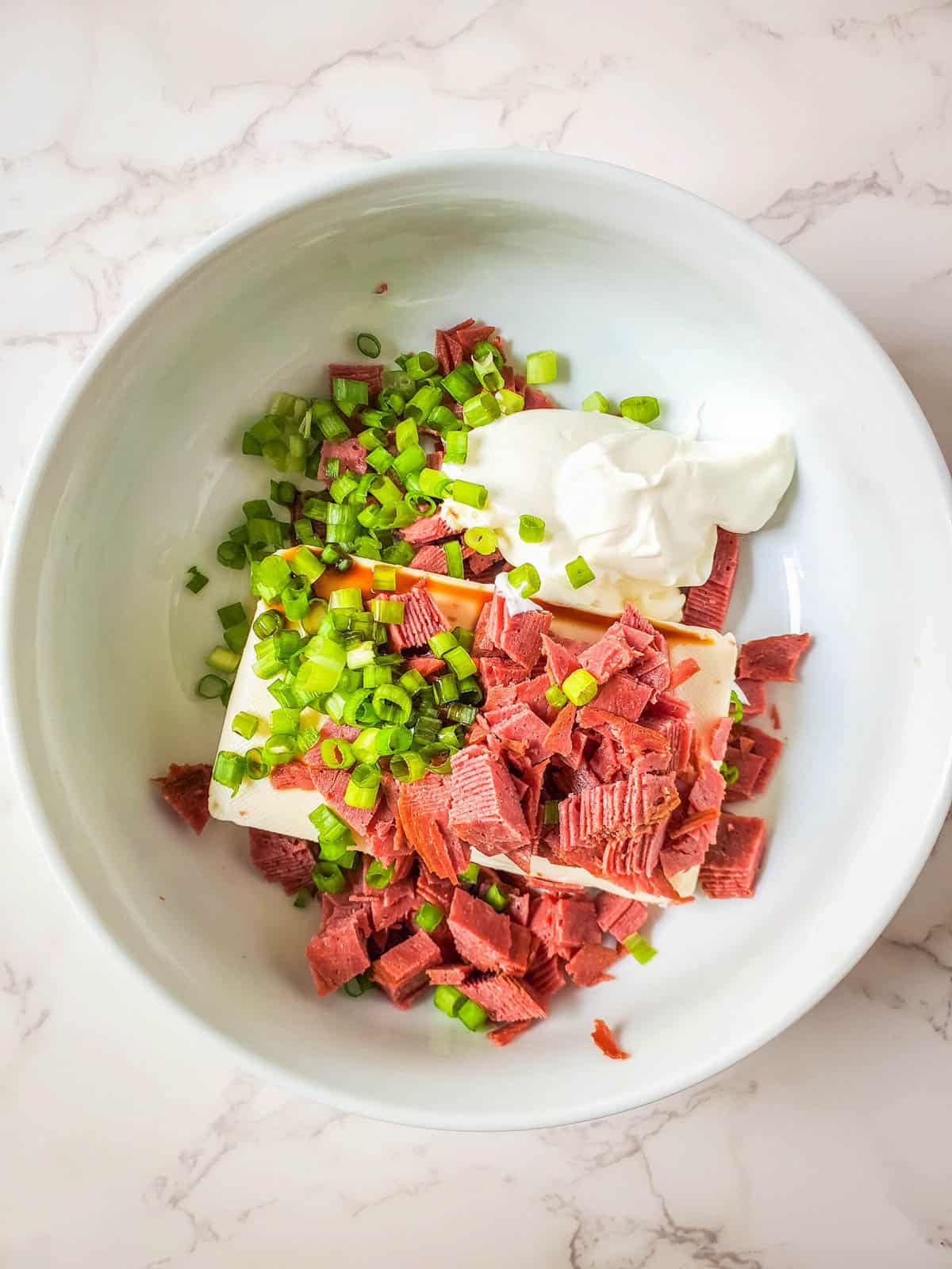 Small pieces of dried beef, a block of softened cream cheese, green onions, and soy sauce altogether in a large bowl.