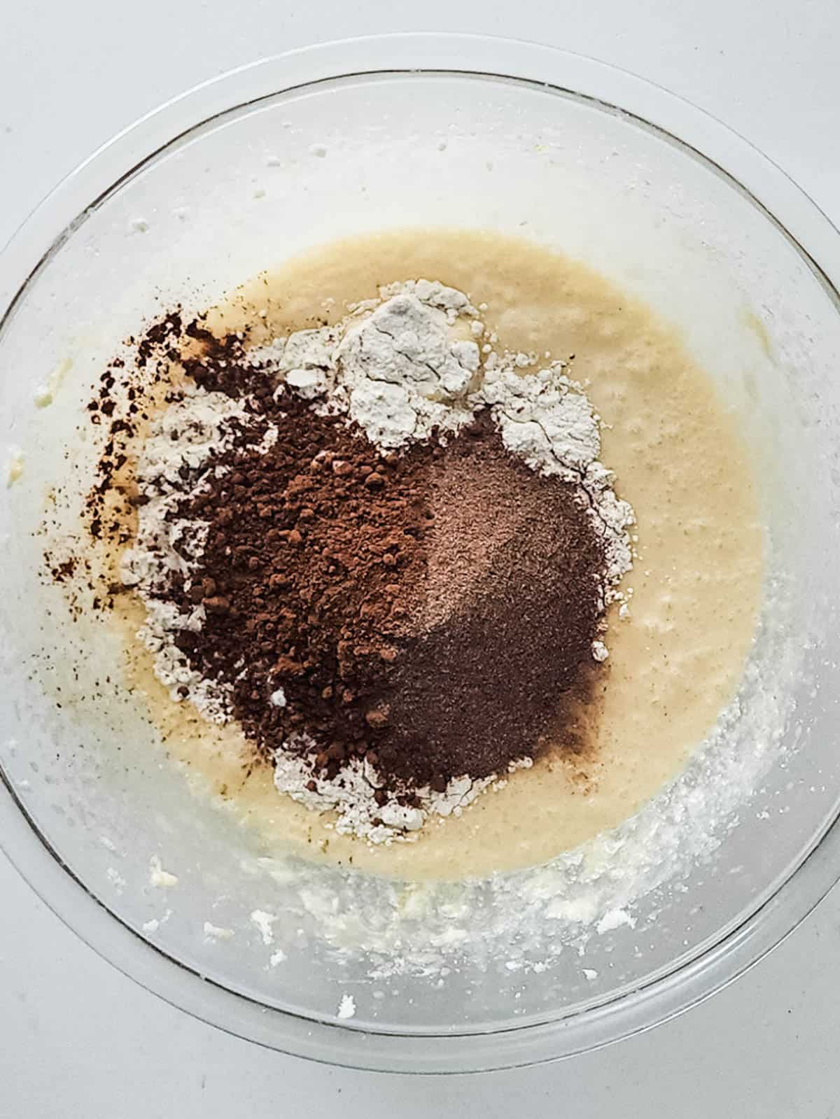 A bowl with cupcake batter with dry cocoa powder and hot chocolate mix before being mixed.