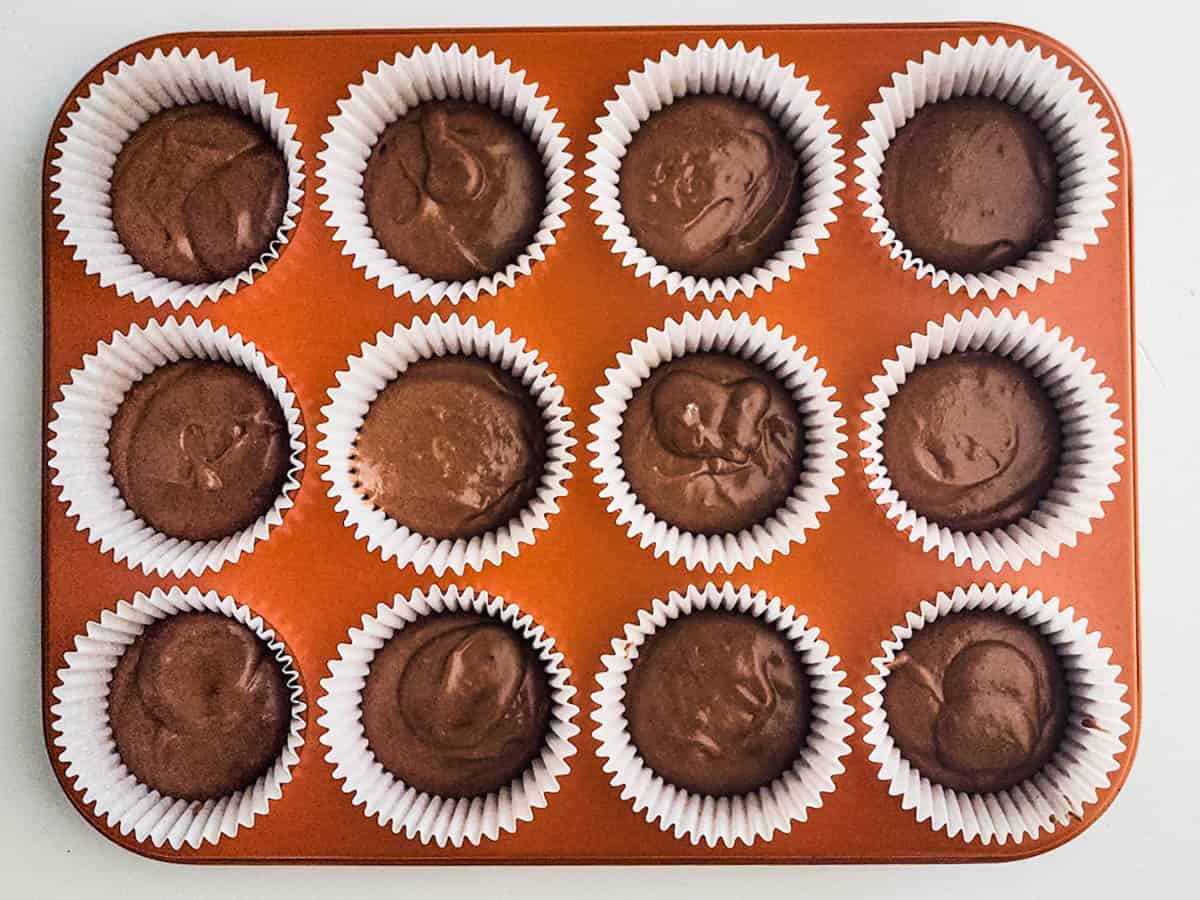 A cupcake pan with liners and hot chocolate cupcake batter before baking.