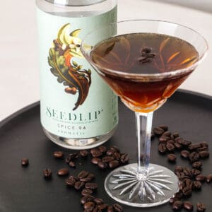 A Non-Alcoholic Espresso Martini in a martini glass on a tray next to a bottle of Seedlip.