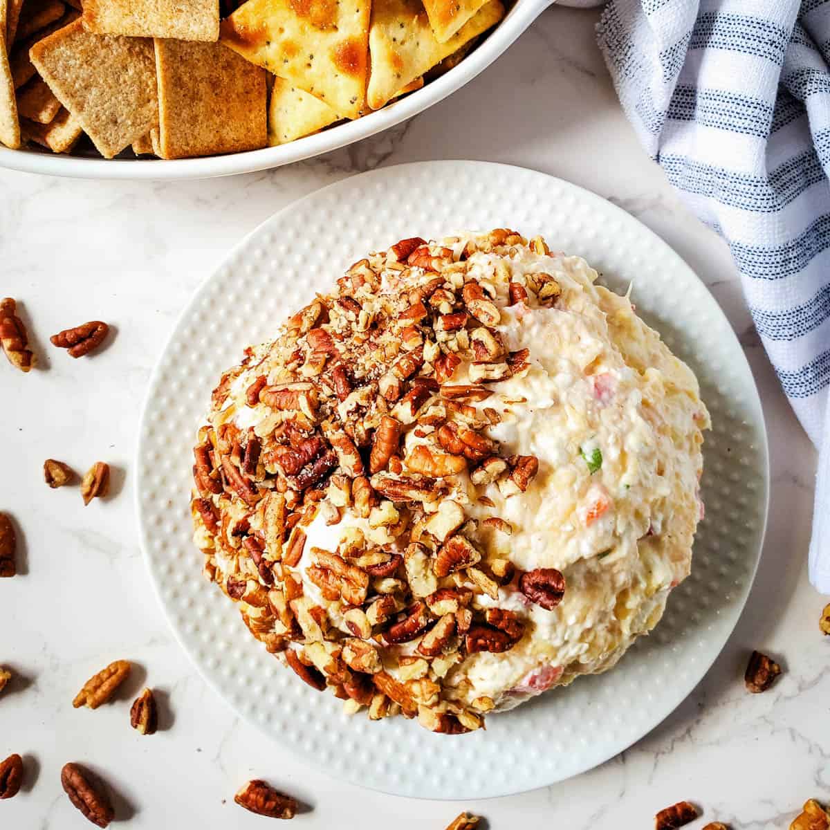 Delicious cream cheese ball with pineapple served on a white plate with crackers in a bowl on the side.