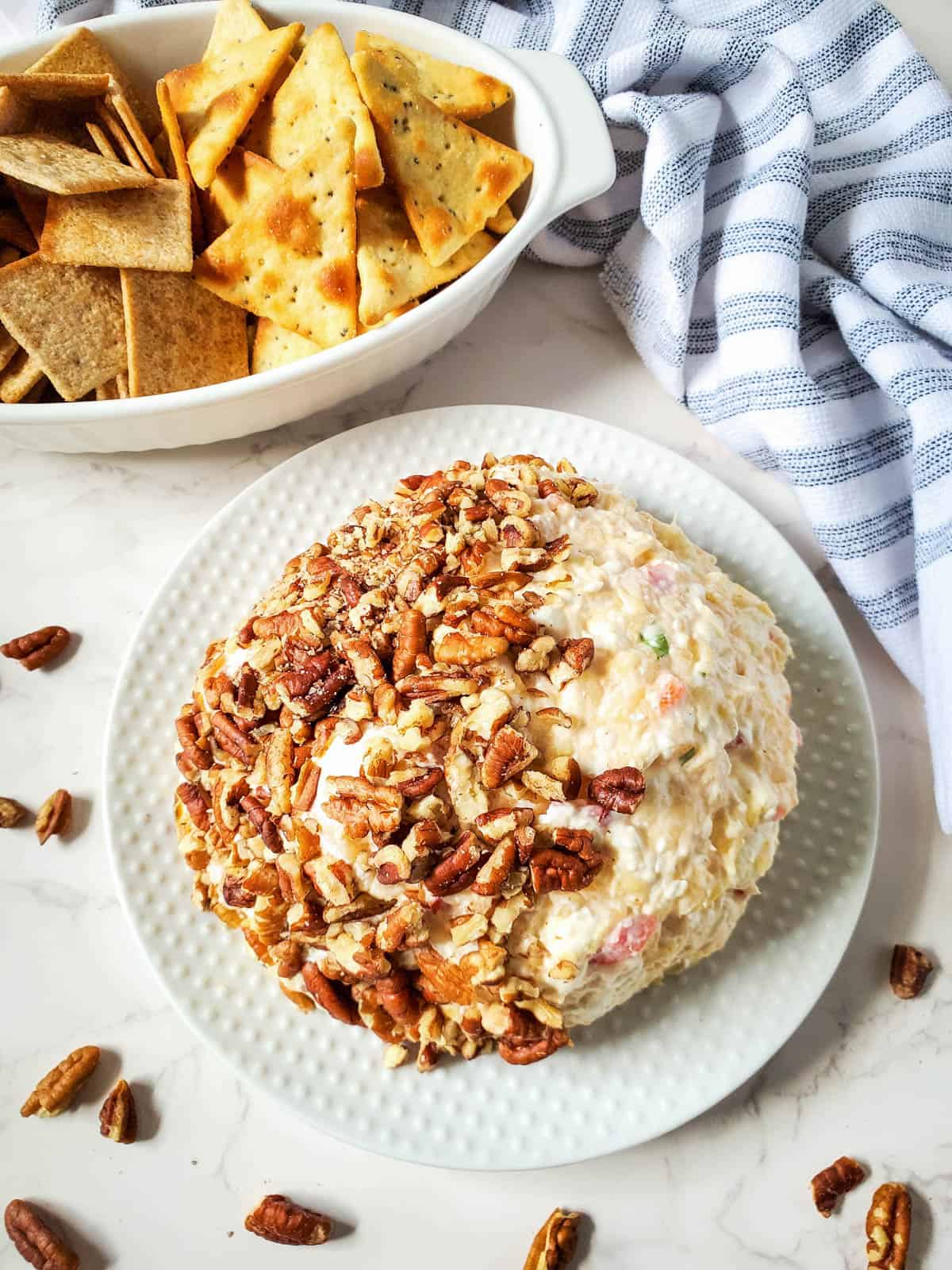 A pineapple cheese ball half coated with pecan nuts on a serving platter with crackers on the side.