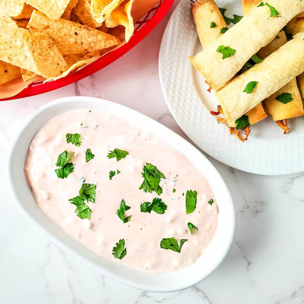 Salsa and sour cream dip topped with cilantro with tortilla chips and taquitos on the side.