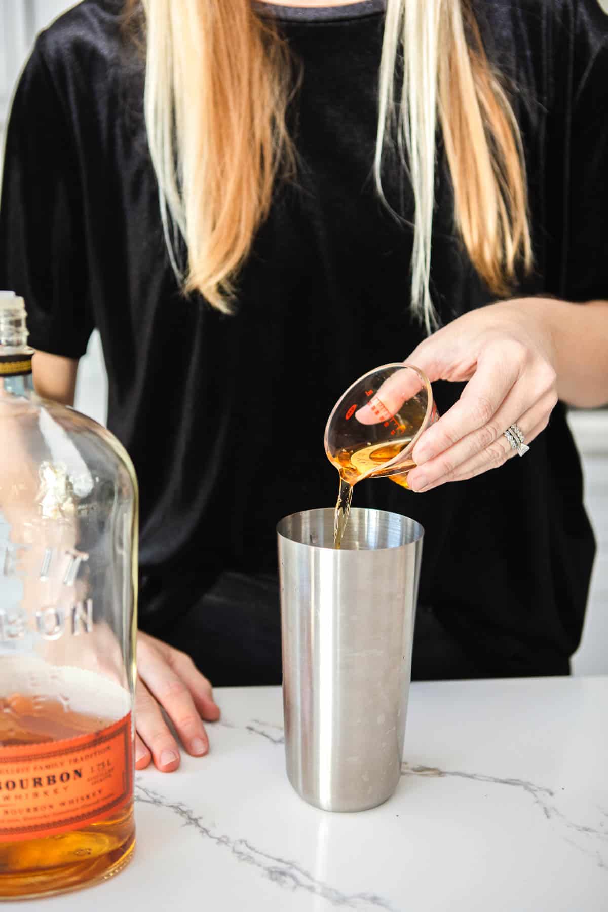 Woman pouring bourbon into a cocktail shaker.