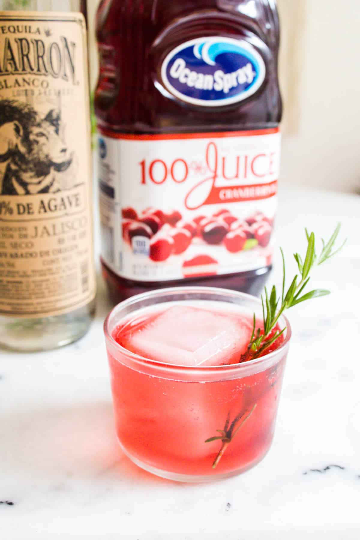 Cranberry juice cocktail in front of bottles of tequila and cranberry juice.