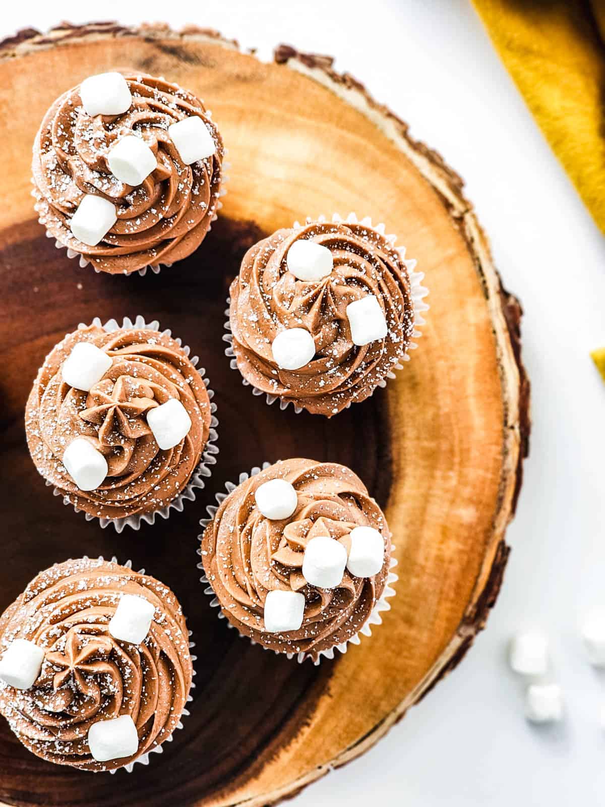 A wooden tray holding mini marshmallow topped frosted hot chocolate cupcakes.