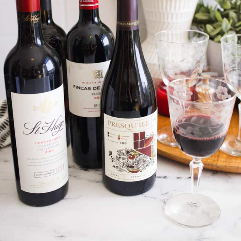 Close up of red wine in a wine glass on a table next to some bottles of wine.