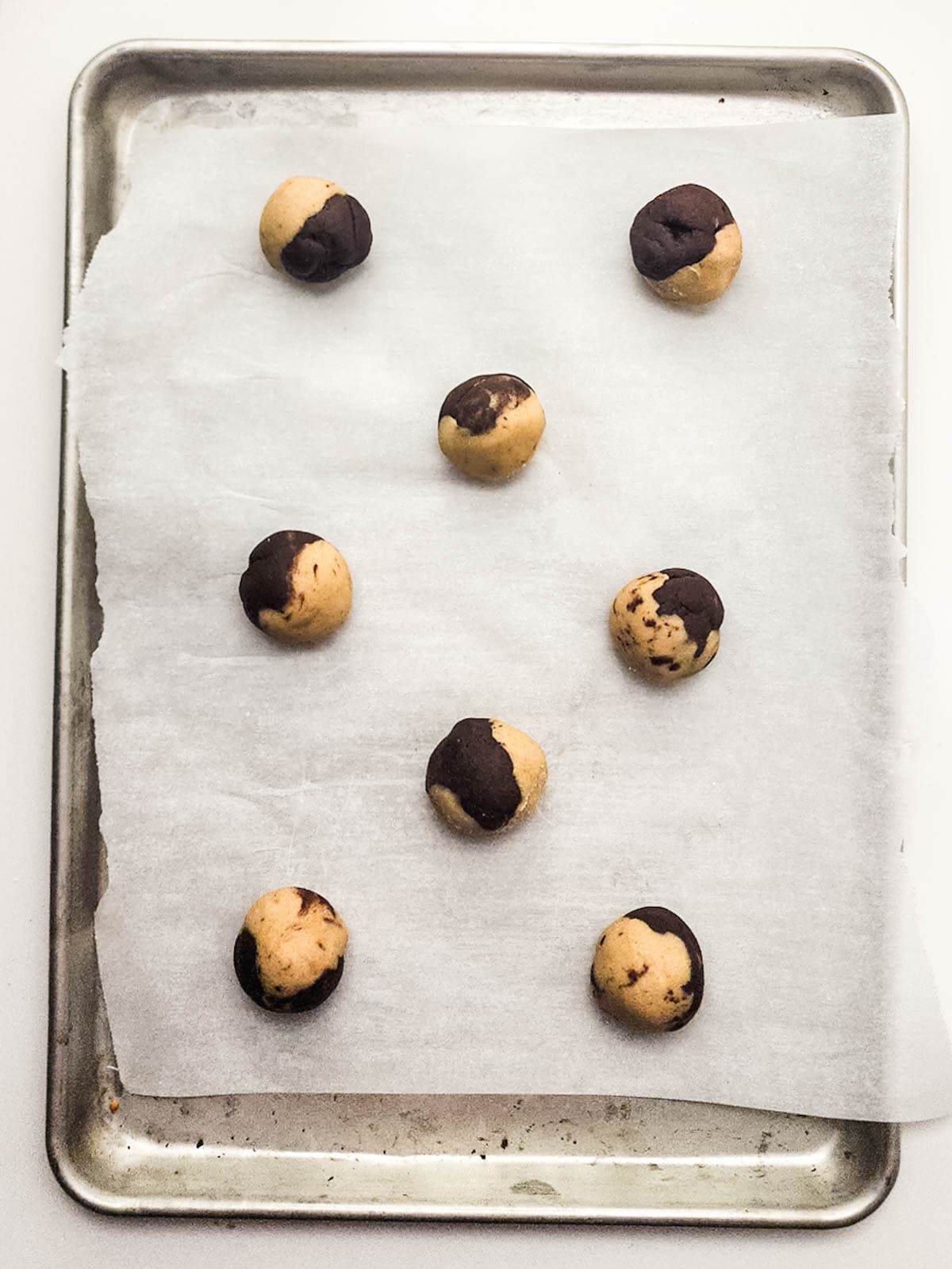 Marble cookie dough balls laid on a baking sheet lined with parchment paper.