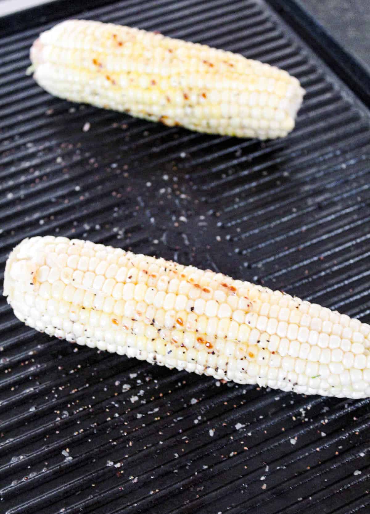 Two corn cobs on the grill with grill marks.