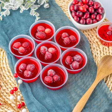 Cranberry Jello Shots on a blue towel topped with sugar cranberries.