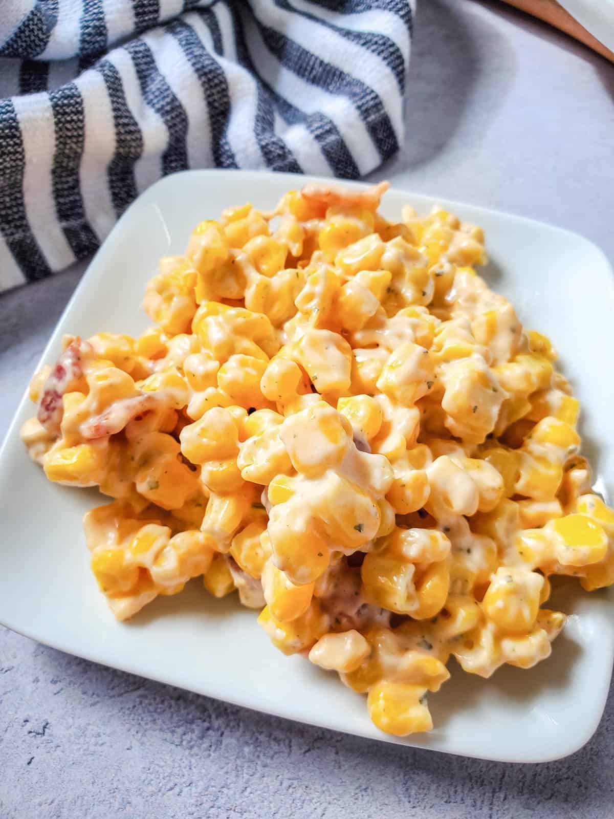 Close up of a white plate with a portion of a creamed corn side dish with bacon.